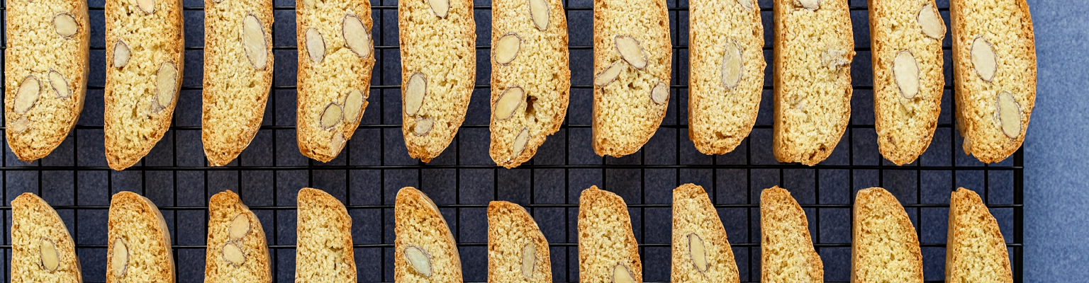 Freshly baked almond biscotti arranged neatly on a black cooling rack against a blue background.