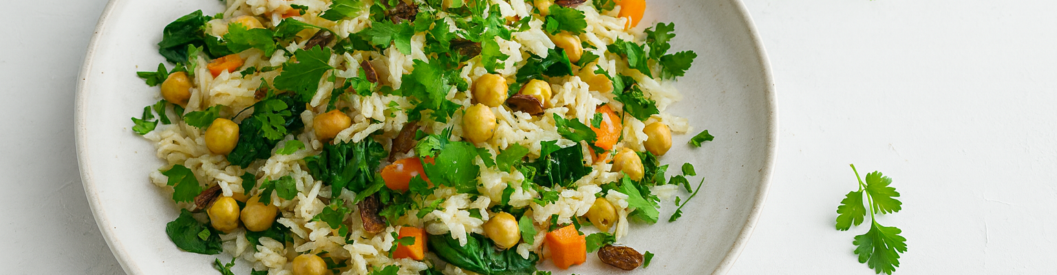 Chickpea rice pilaf with carrots, spinach, raisins, and fresh coriander served on a white plate.
