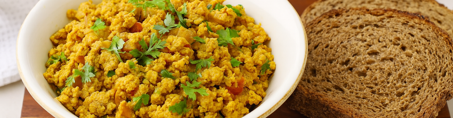 Egg bhurji with capsicum, tomato, and onion garnished with fresh coriander, served with whole grain bread.