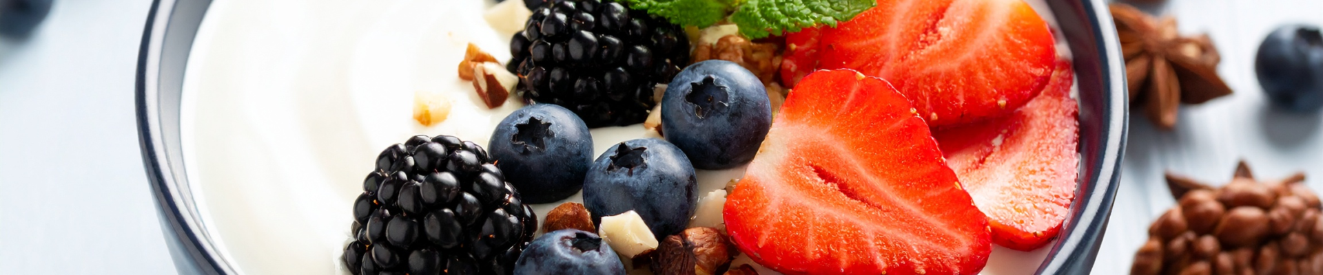 Greek yoghurt topped with fresh strawberries, blueberries, blackberries, nuts, and mint leaves in a bowl.