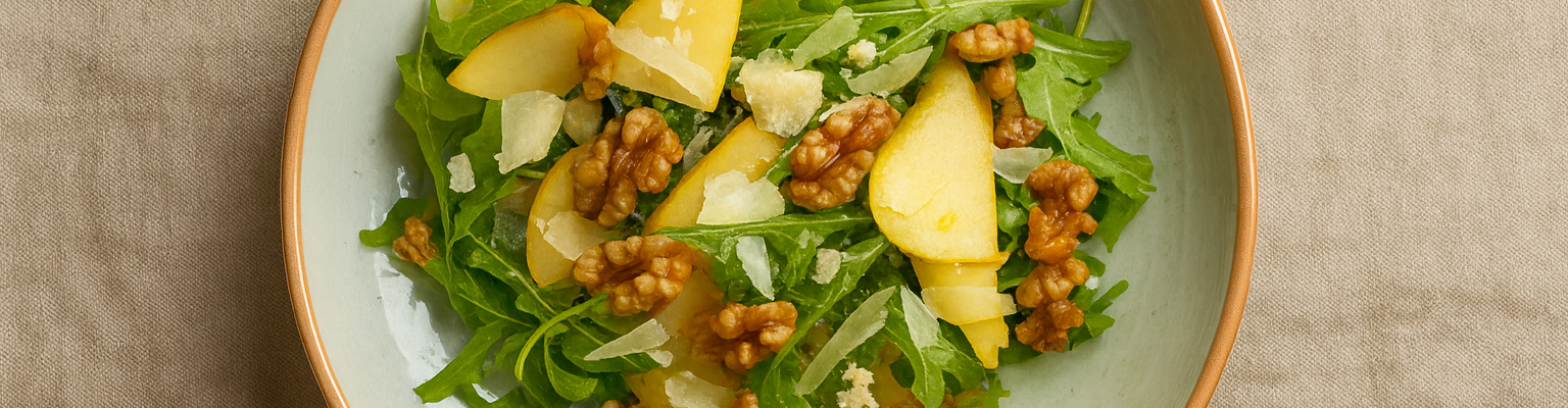 Fresh pear, walnut, and rocket salad topped with shaved parmesan on a rustic plate.