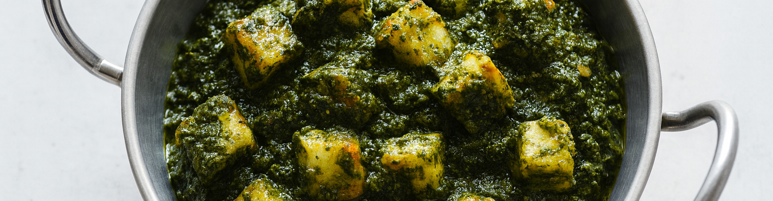 Stainless-steel karahi filled with saag paneer—golden paneer cubes in a thick spiced spinach sauce, photographed from above.