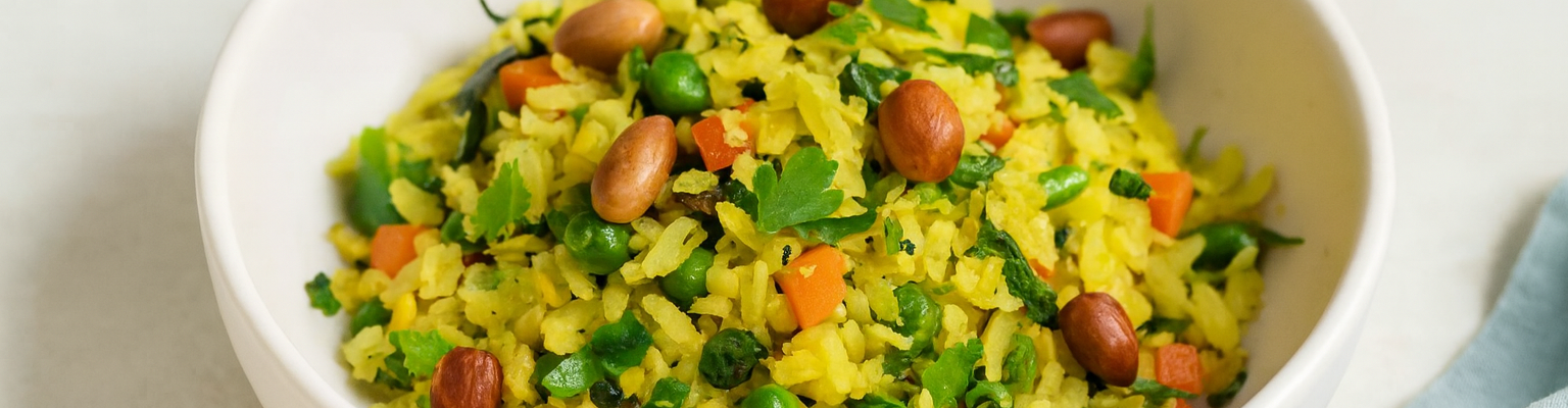 Vegetable poha with carrots, peas, curry leaves, coriander, and roasted peanuts served in a bowl.