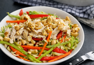 A bowl of chicken noodle salad with shredded chicken, sliced vegetables and roasted cashews.
