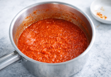 A saucepan of tomato-based sauce with a rich red colour, sitting on a light marble surface.